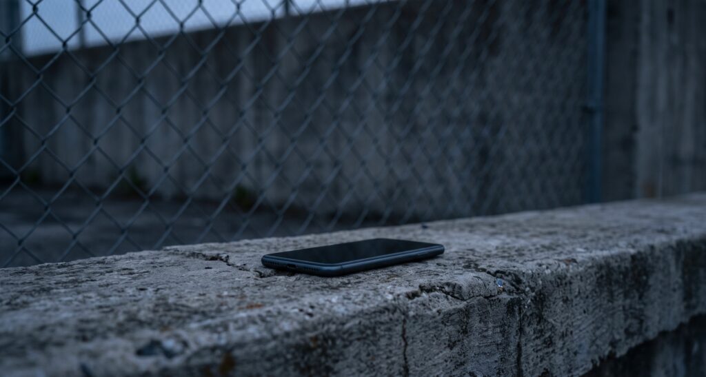 Florida's New Criminal Gang Member Definition: What HB 429 Changes A closed smartphone lying face down on a concrete ledge in front of a chain-link fence at dusk
